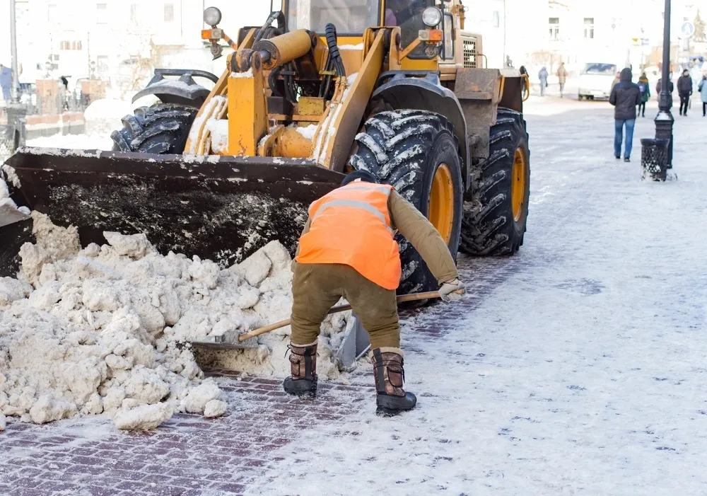 Worker shoveling snow near snowplow.