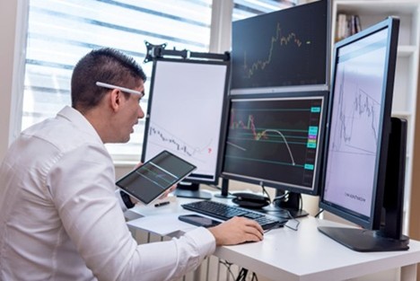 Streesed Man at shallow desk with multiple and large monitors