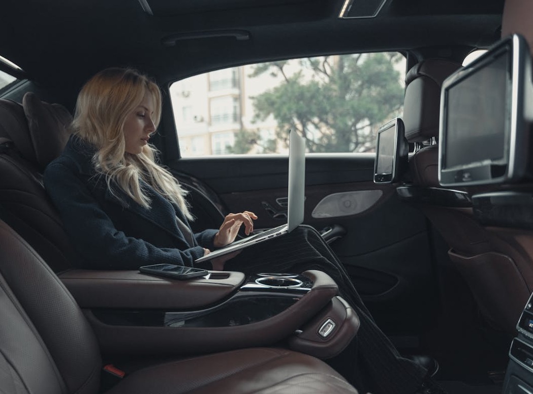 woman working on laptop from rear of a luxury car