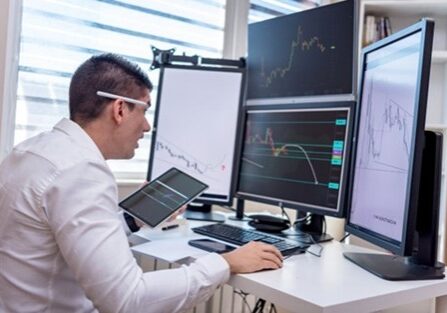 Streesed Man at shallow desk with multiple and large monitors