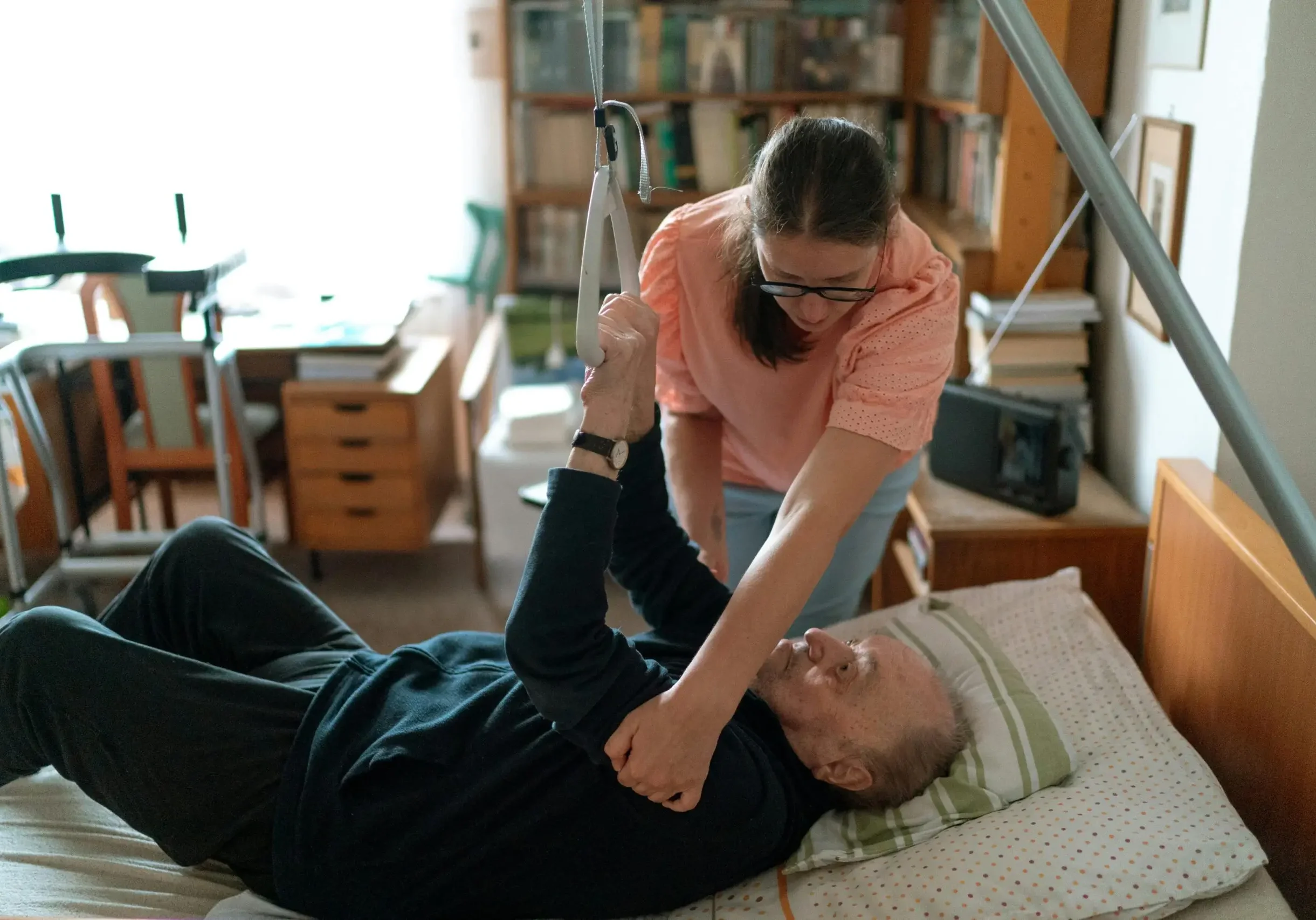 Caregiver assisting elderly man in bed.