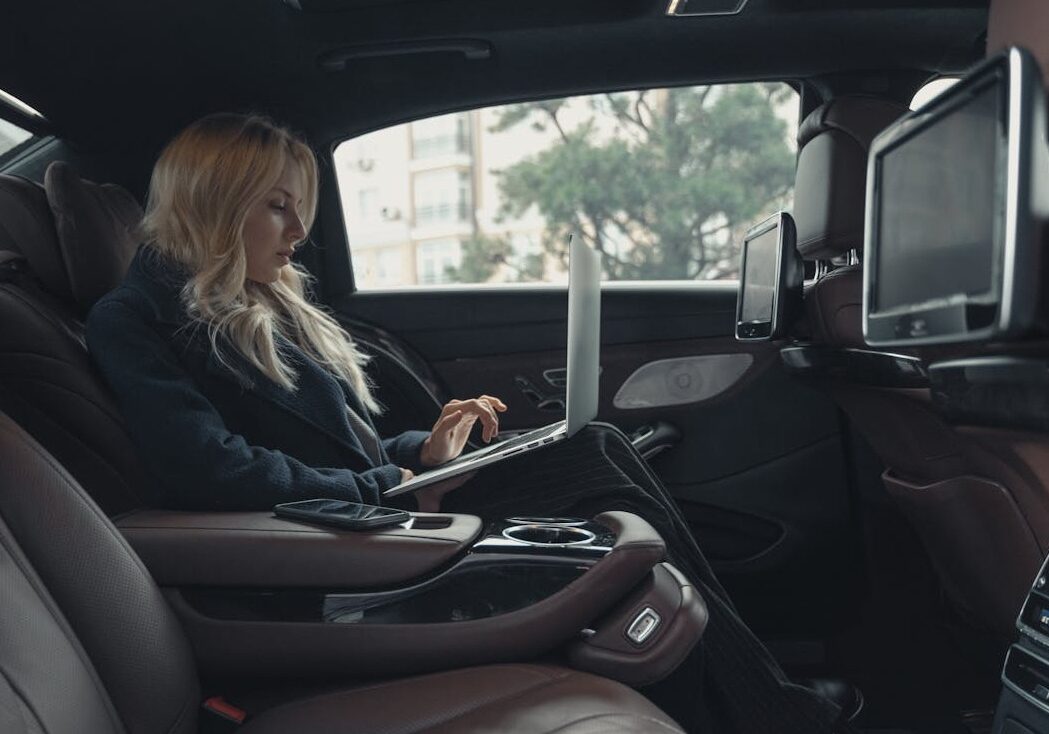 woman working on laptop from rear of a luxury car